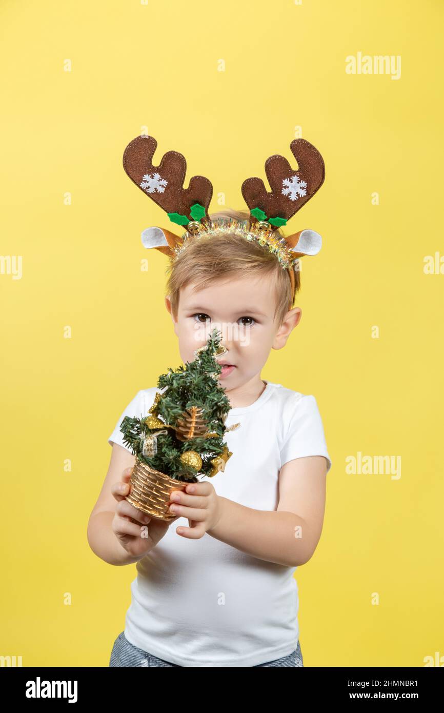 Felice ragazzo divertente bambino in rosso costume di renna di Natale con albero decorativo di natale su sfondo giallo Foto Stock