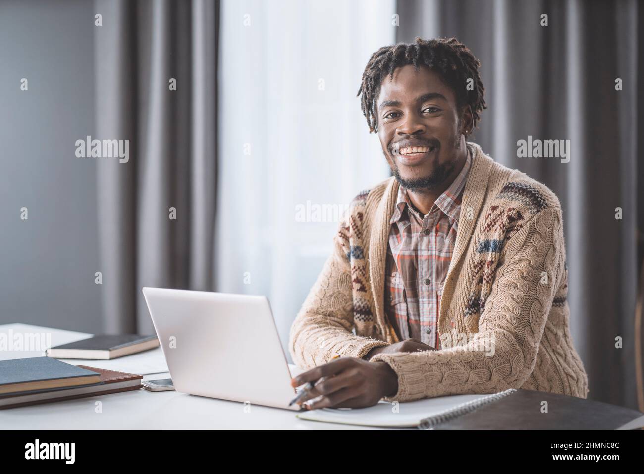 Studentessa afroamericana studia da casa utilizzando un computer portatile seduto accanto alla finestra. Giovane imprenditore che lavora sul suo portatile a casa. Studio di studenti afroamericani a casa durante il blocco. Foto Stock