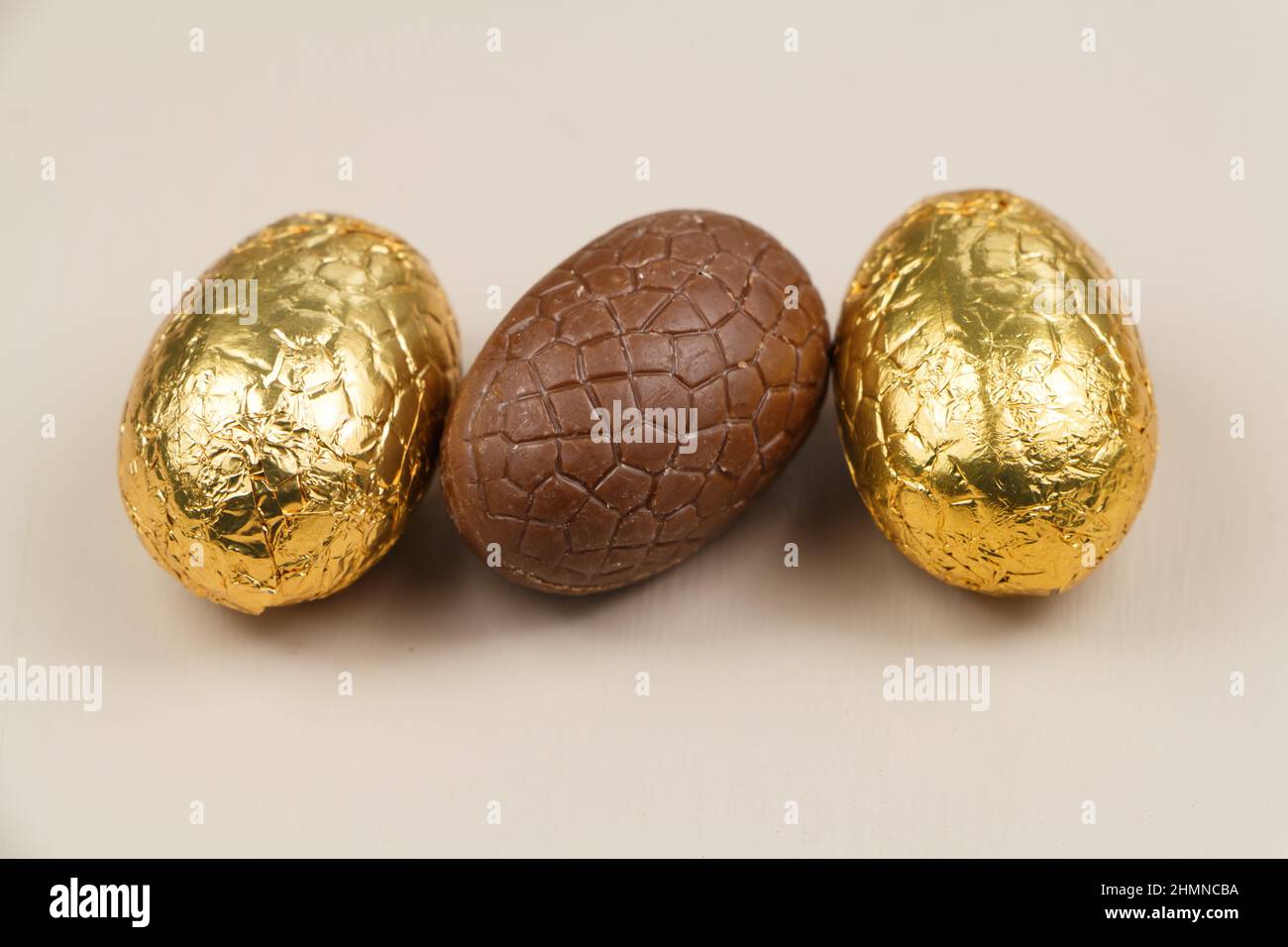 Tre uova di cioccolato al latte avvolte in carta dorata per pasqua Foto Stock