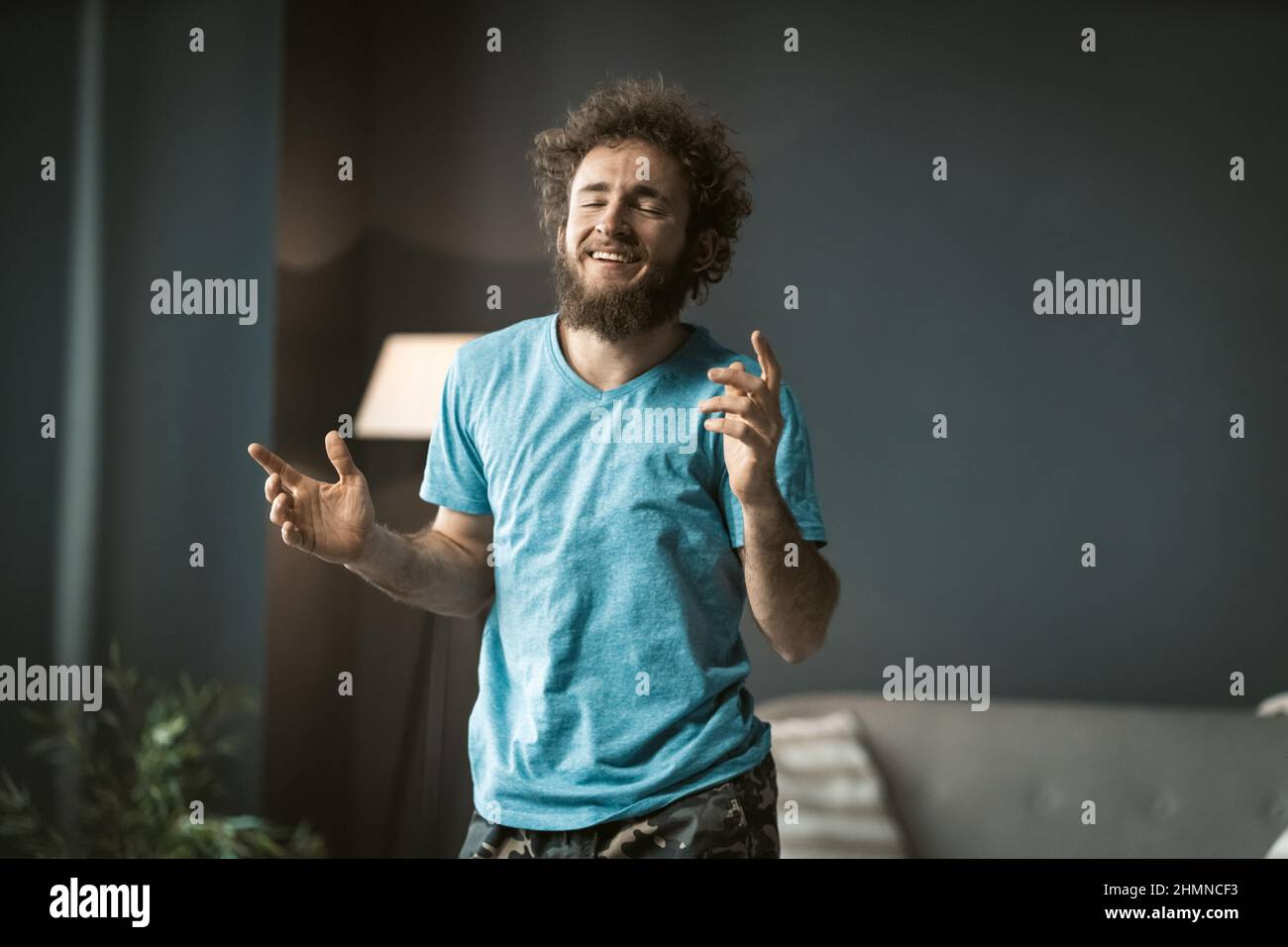 Rilassato giovane disheveled uomo stretching in danza dopo un lungo ore di lavoro distanza durante la quarantena rimanendo a casa. Giovane bel freelance a casa godendo di tempo libero. Foto Stock