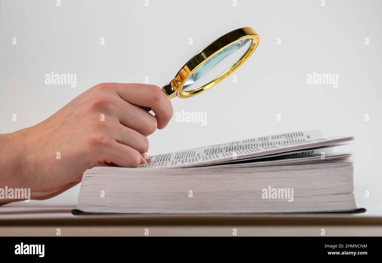 Tenere la lente di ingrandimento sul libro aperto. Studio, concetto di ricerca. Foto di alta qualità Foto Stock