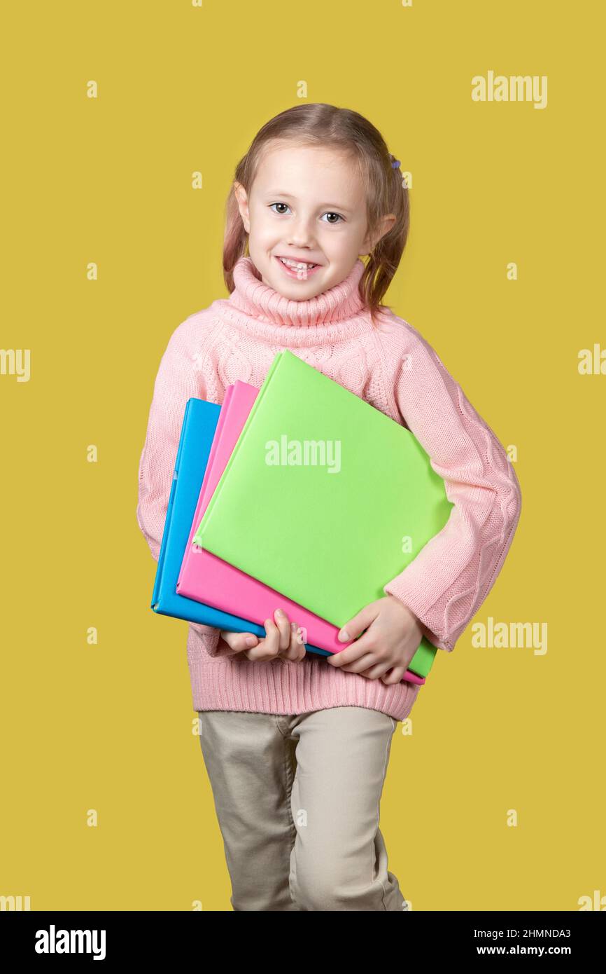 Ritratto della ragazza felice della scuola di età elementare sorridente e guardando la macchina fotografica su sfondo giallo. Foto Stock
