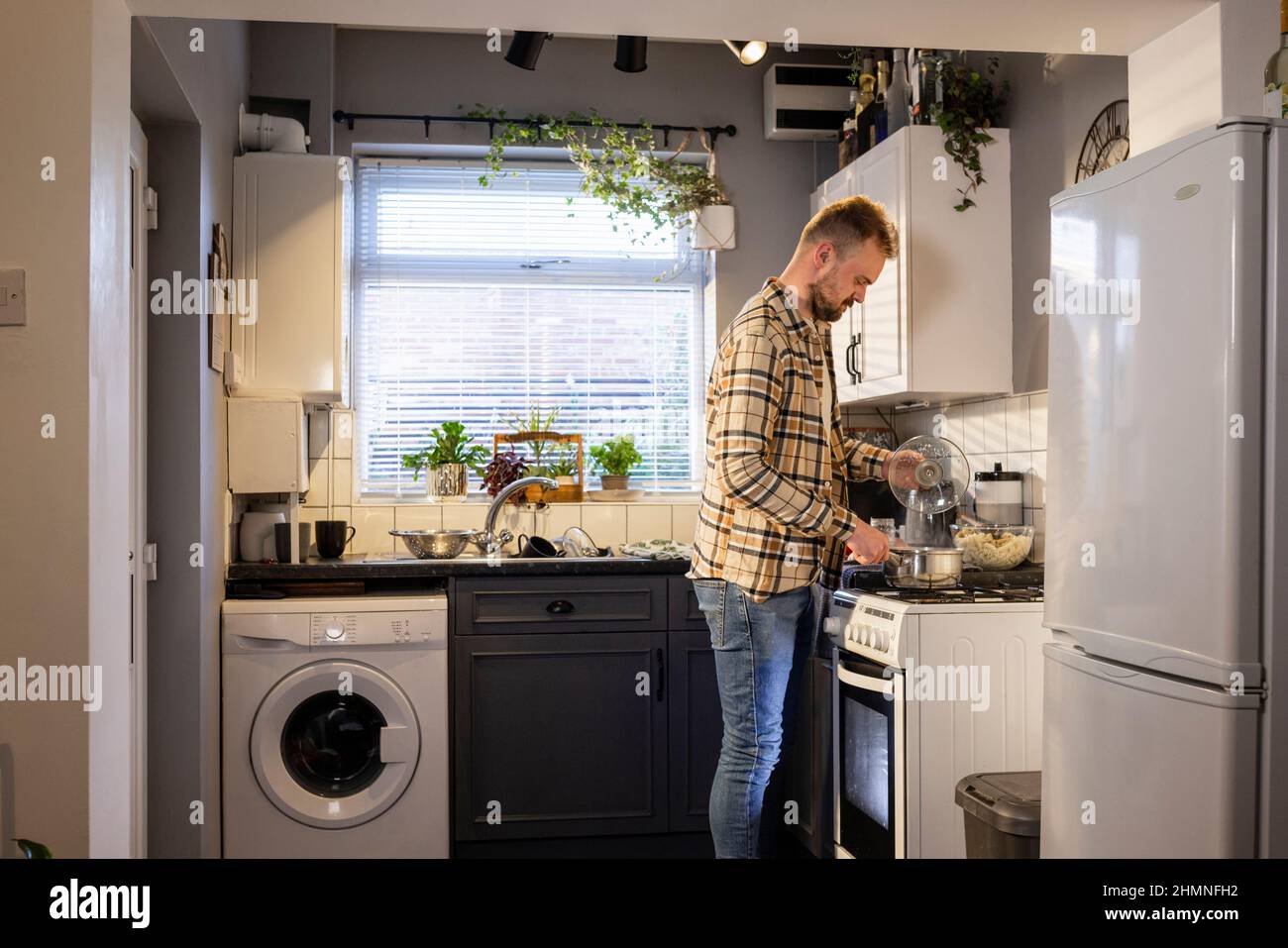 Un colpo di vista laterale di un uomo caucasico in piedi nella sua cucina, sta facendo la pasta per il pranzo. Foto Stock