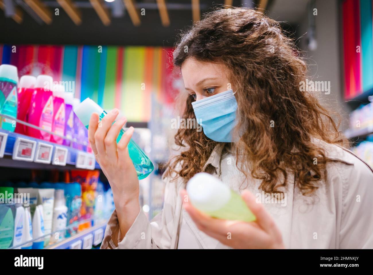 Ritratto di donna shopper con capelli ricci indossare maschera medica in supermercato sceglie shampoo durante l'epidemia di coronavirus Foto Stock