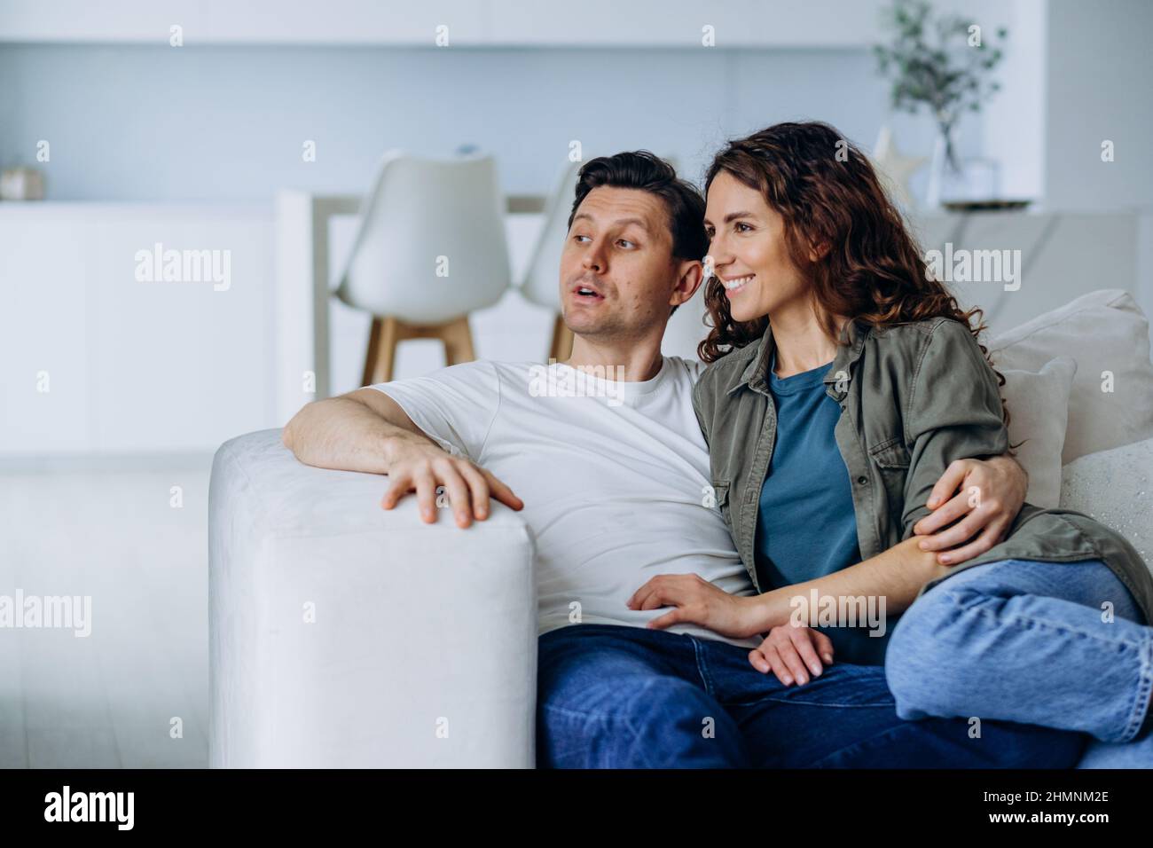 Sposi felici con capelli scuri sedersi su un comodo divano in soggiorno e discutere i piani per il futuro sorridendo ampiamente primo piano Foto Stock