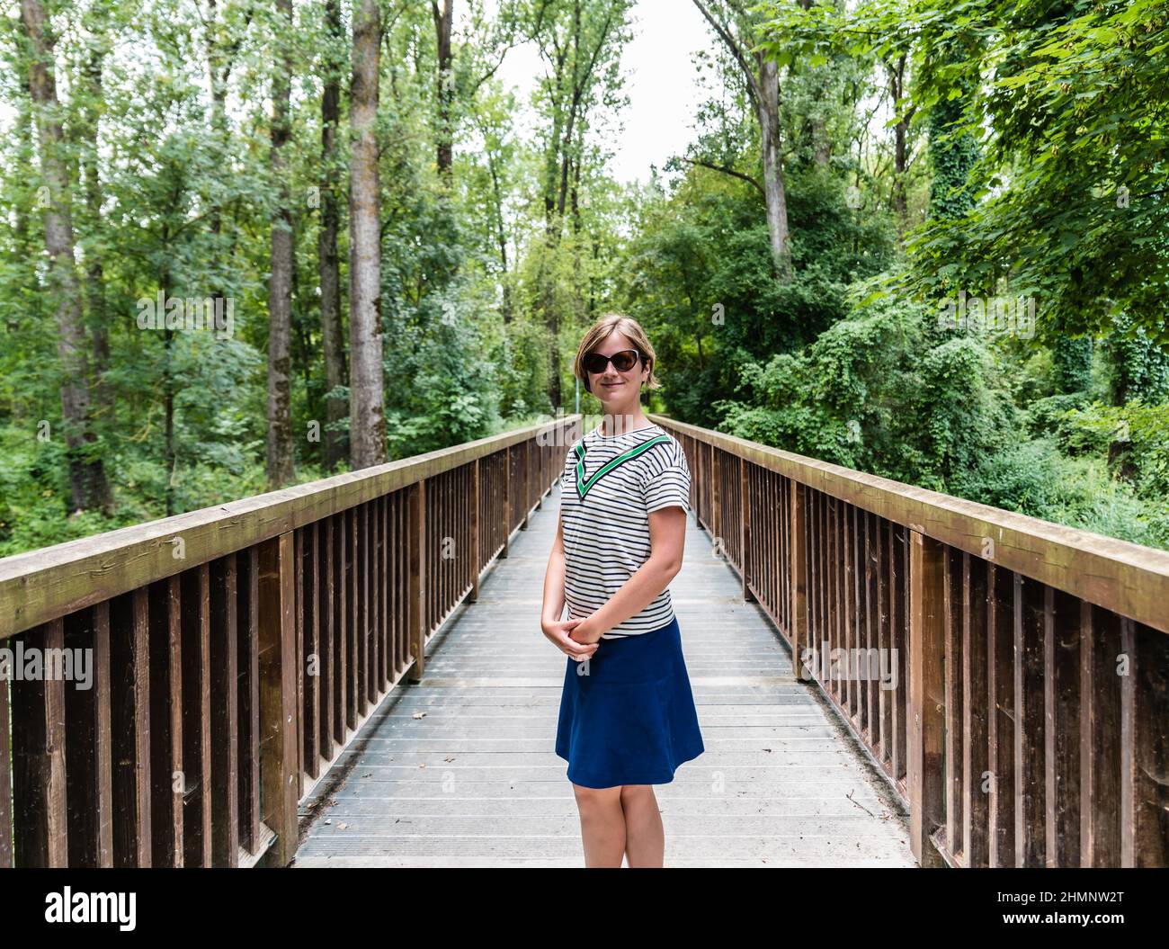 ritratto di una donna bianca di 30 anni in un abito estivo in piedi su un ponte pedonale di legno Foto Stock