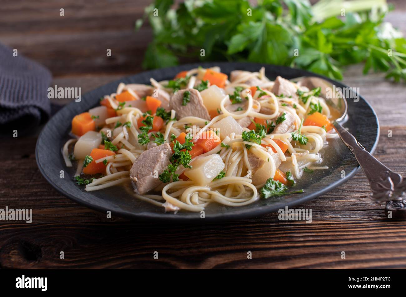 Zuppa di spaghetti di pollo su un piatto scuro con cucchiaio isolato su un tavolo di legno Foto Stock