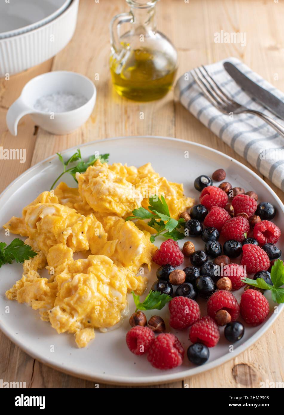 Piatto colazione a base di carb con uova strapazzate servito con bacche fresche e nocciole su tavola di legno di pino. Immagine verticale Foto Stock