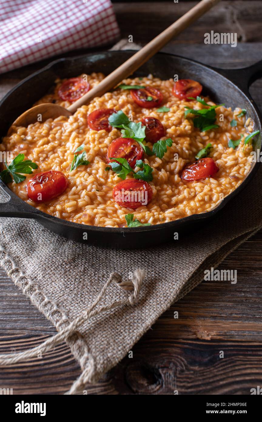 Risotto tradizionale con pomodori e parmigiano. Servito in una rustica teglia in ghisa su un tavolo di legno. Primo piano, immagine verticale con spazio di copia Foto Stock