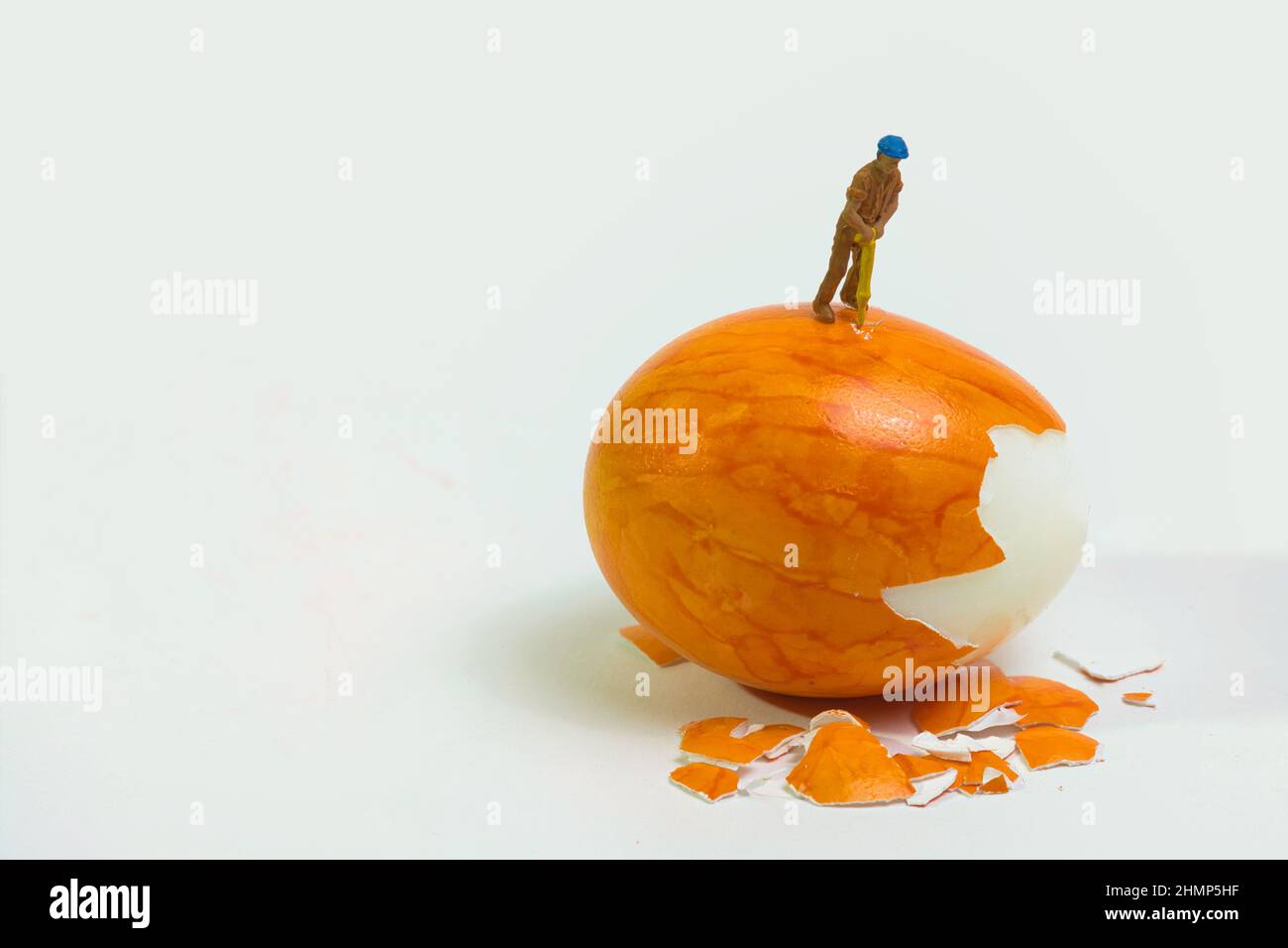 un operatore con un martello idraulico si trova sopra un uovo arancione per sbucciarlo Foto Stock