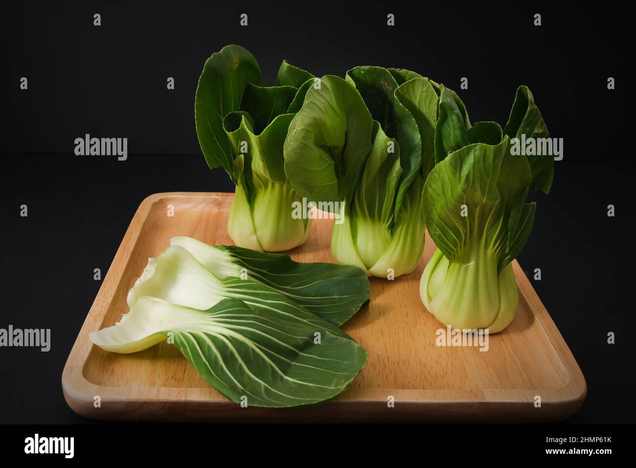 Bianco biologico Baby Bok Choy o Brassica rapa chinensis su piastra di legno su sfondo nero. Foto Stock