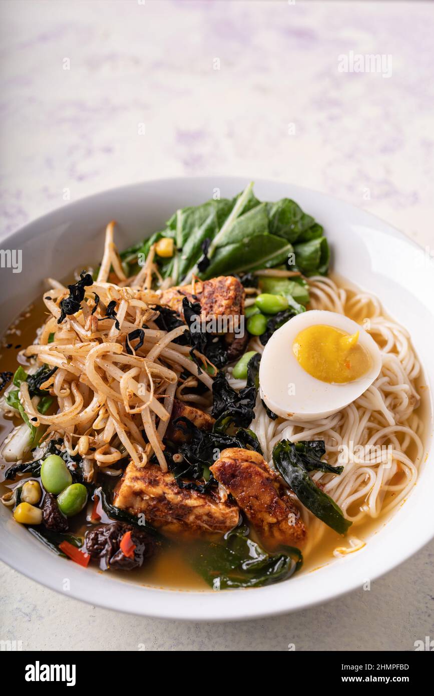 Spaghetti di ramen senza carne di vegano a fusione asiatica con funghi, tofu fermentato, germogli, fagioli, uova di vegan e foglie verdi di pak choi Foto Stock