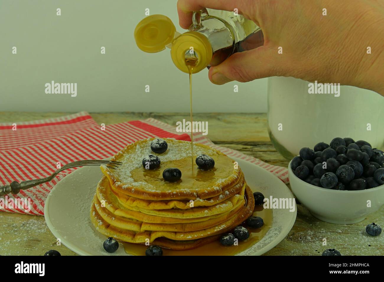 Primo piano di versare lo sciroppo d'acero su una pila di pancake. Impila di pancake con mirtilli freschi versati con sciroppo d'acero Foto Stock