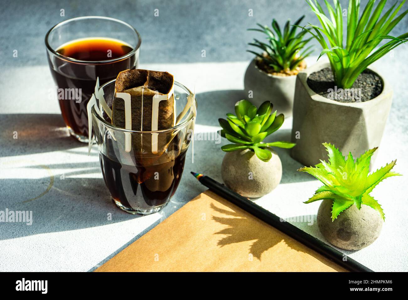 Filtro del caffè individuale e bevanda di caffè vicino alle piante domestiche, al blocco note e alla matita Foto Stock