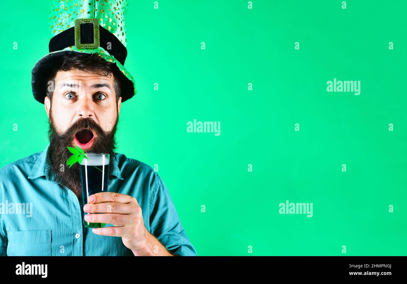 Uomo con bicchiere di birra con shamrock. San Patrizio. Sorprendo maschio in berretto leprechaun. Foto Stock