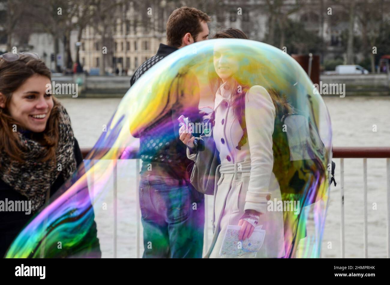 Un artista di strada sul lungofiume del Tamigi a Londra, Regno Unito, rilascia grandi bolle. Turisti femminili che guardano una grande bolla traslucida Foto Stock