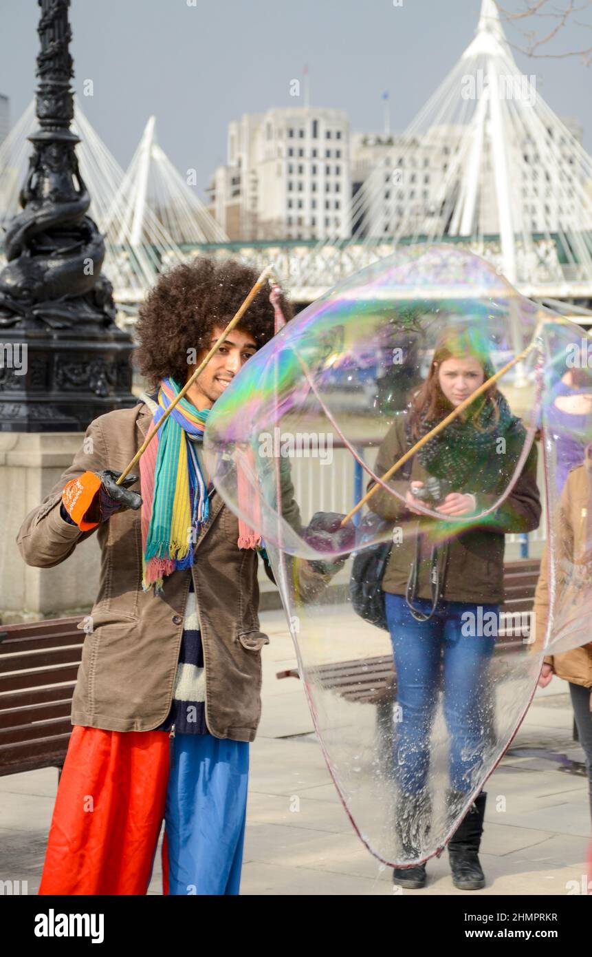 Un artista di strada sul lungofiume del Tamigi a Londra, Regno Unito, rilascia bolle da un cerchio. Busker, autobus per soldi da turisti Foto Stock