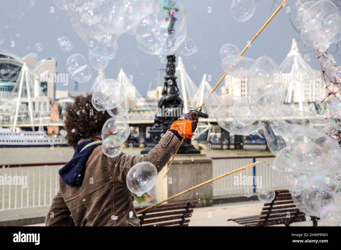 Un artista di strada sul lungofiume del Tamigi a Londra, Regno Unito, rilascia bolle da una rete. Busker, autobus per soldi da turisti Foto Stock