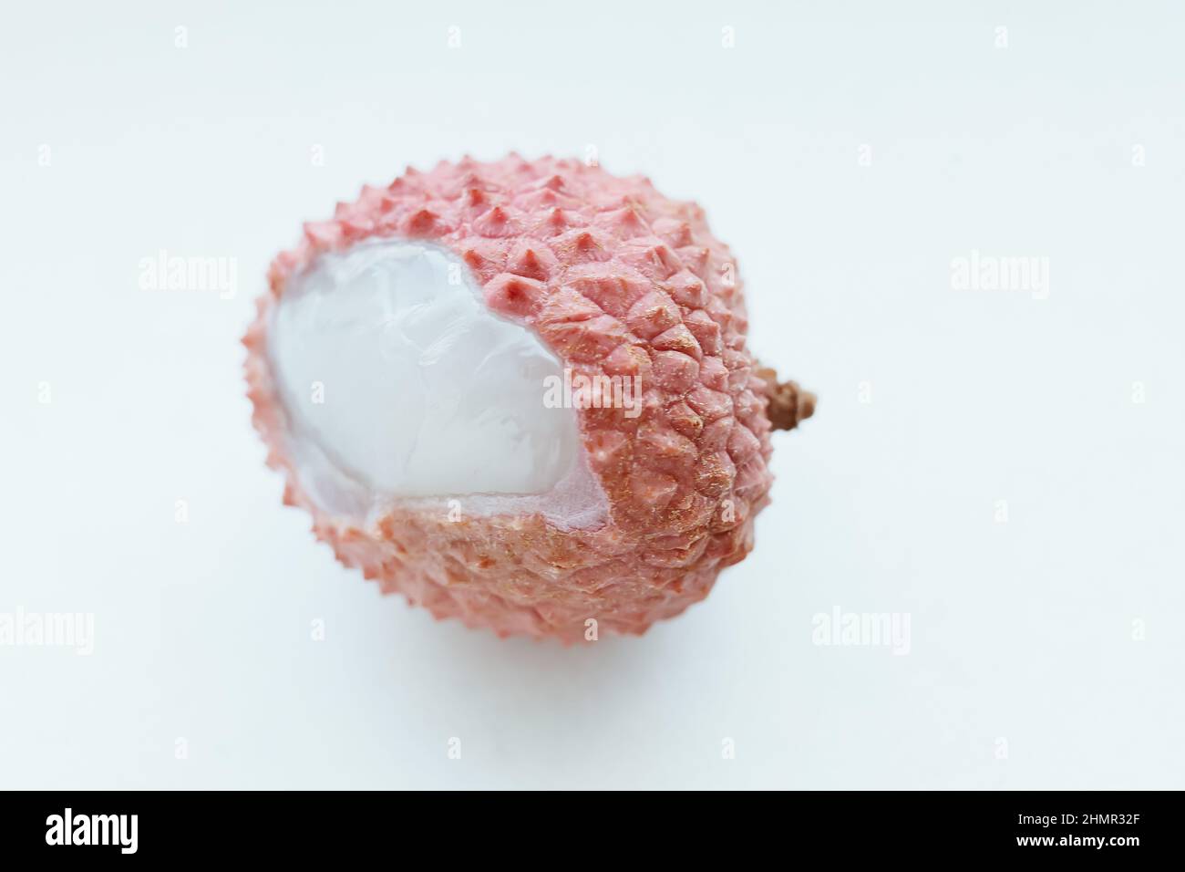 Lychee rosa frutta con guscio testurizzato e morbido succosa polpa macro su sfondo isolato Foto Stock
