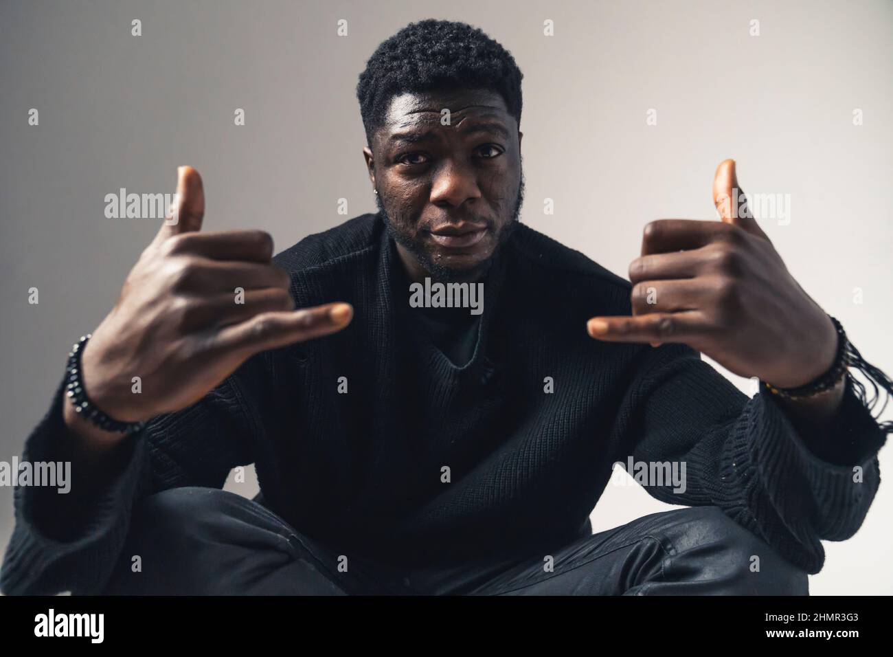 Agghiacciante African American seduta con segno shaka che fissava lo sfondo bianco della fotocamera - ritratto girato. Foto di alta qualità Foto Stock