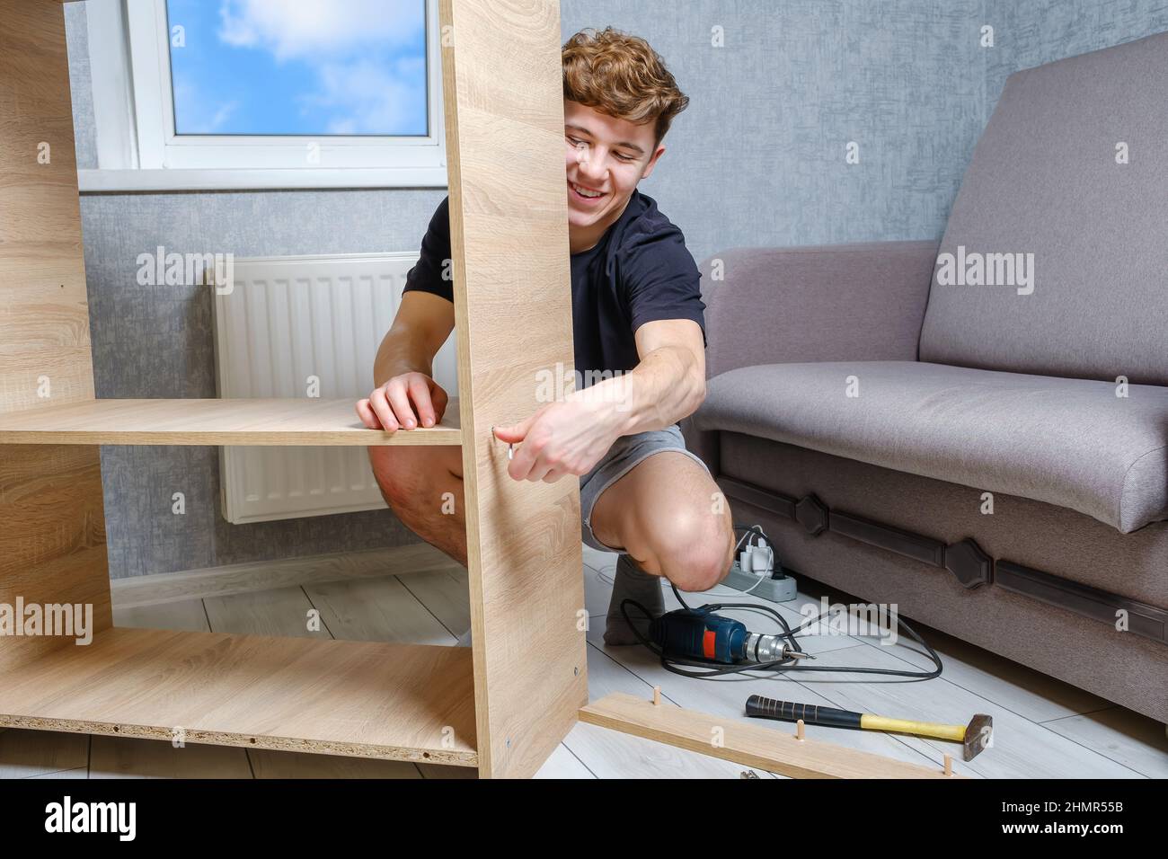 Giovane uomo che lavora con mobili in legno in camera sul pavimento Foto Stock