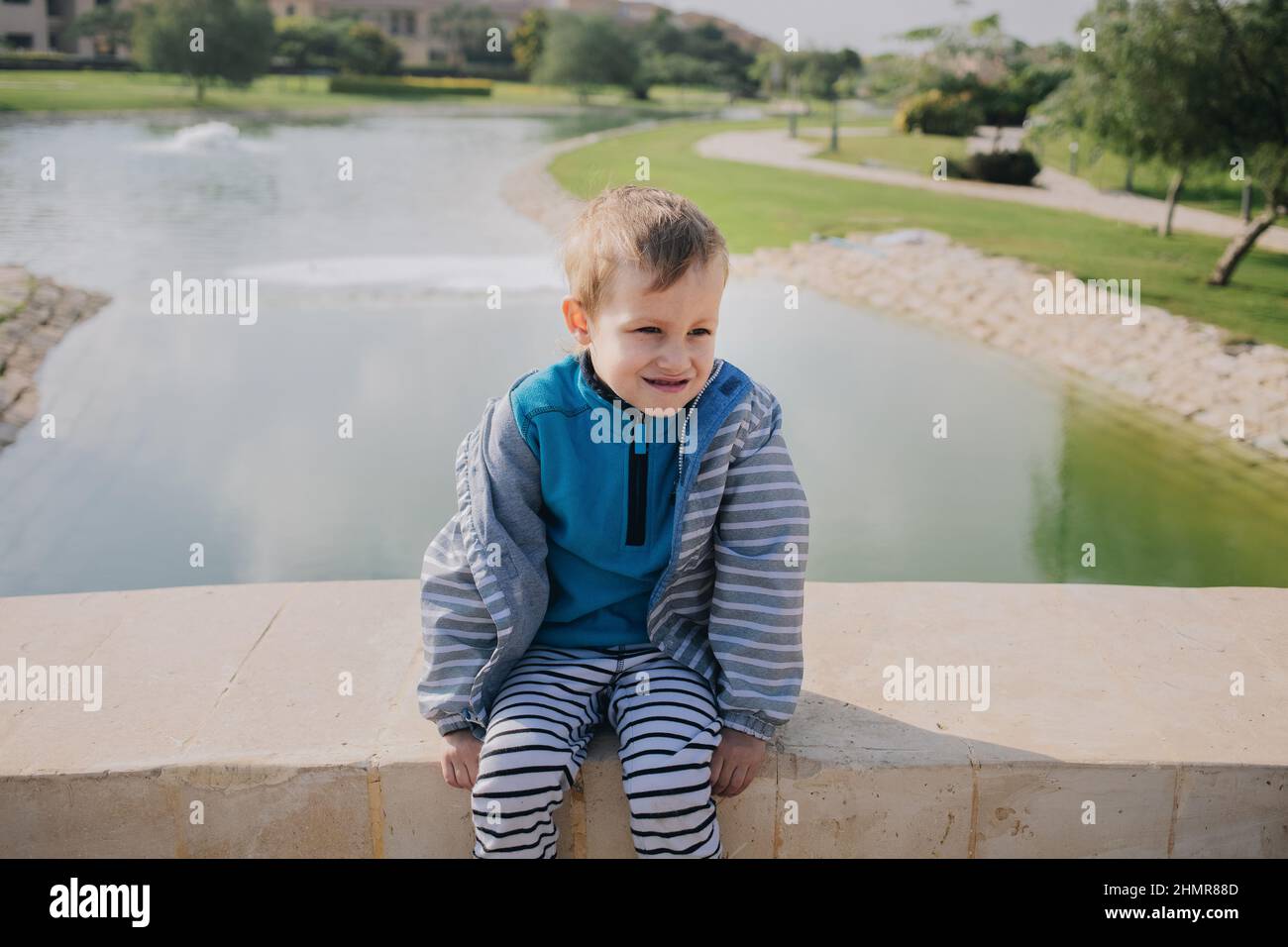 Naughty frolic divertente camminando prescolare bambino si siede al ponte vicino al lago Foto Stock