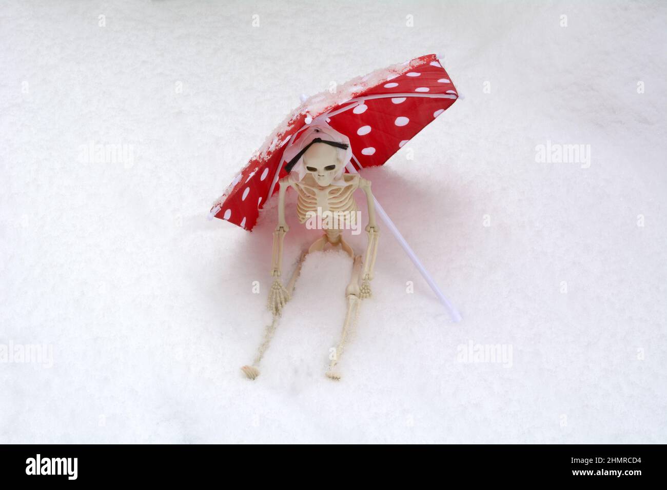 Scheletro seduto protetto da ombrellone rosso con puntini bianchi durante la tempesta di neve Foto Stock