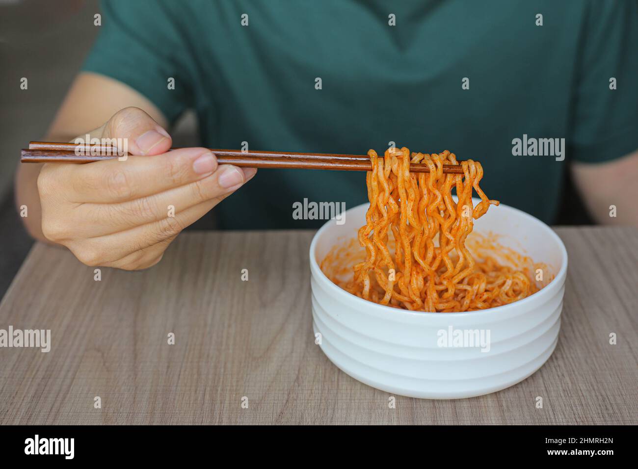 un uomo in una t-shirt verde tiene bacchette con spaghetti istantanei in stile coreano. K-pop è diventato un fenomeno globale che esporta cultura pop, intrattenimento Foto Stock