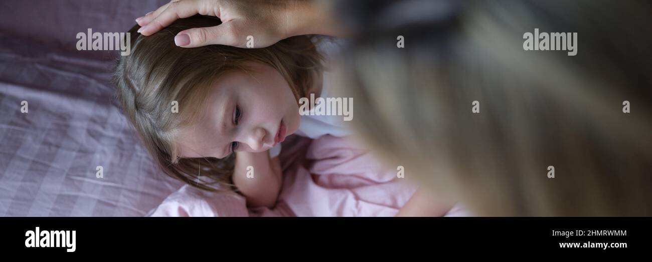 La mamma mette la ragazza triste sulla testa prima di andare a letto. Foto Stock