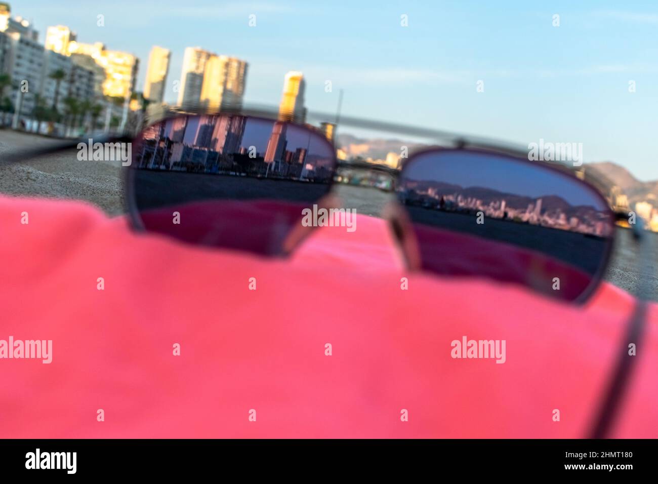 Occhiali da sole vista della città di Benidorm in un asciugamano rosso. Nella spiaggia di Poniente, le torri cittadine viste attraverso un occhiale colorato adagiato in un'ora d'oro. Foto Stock