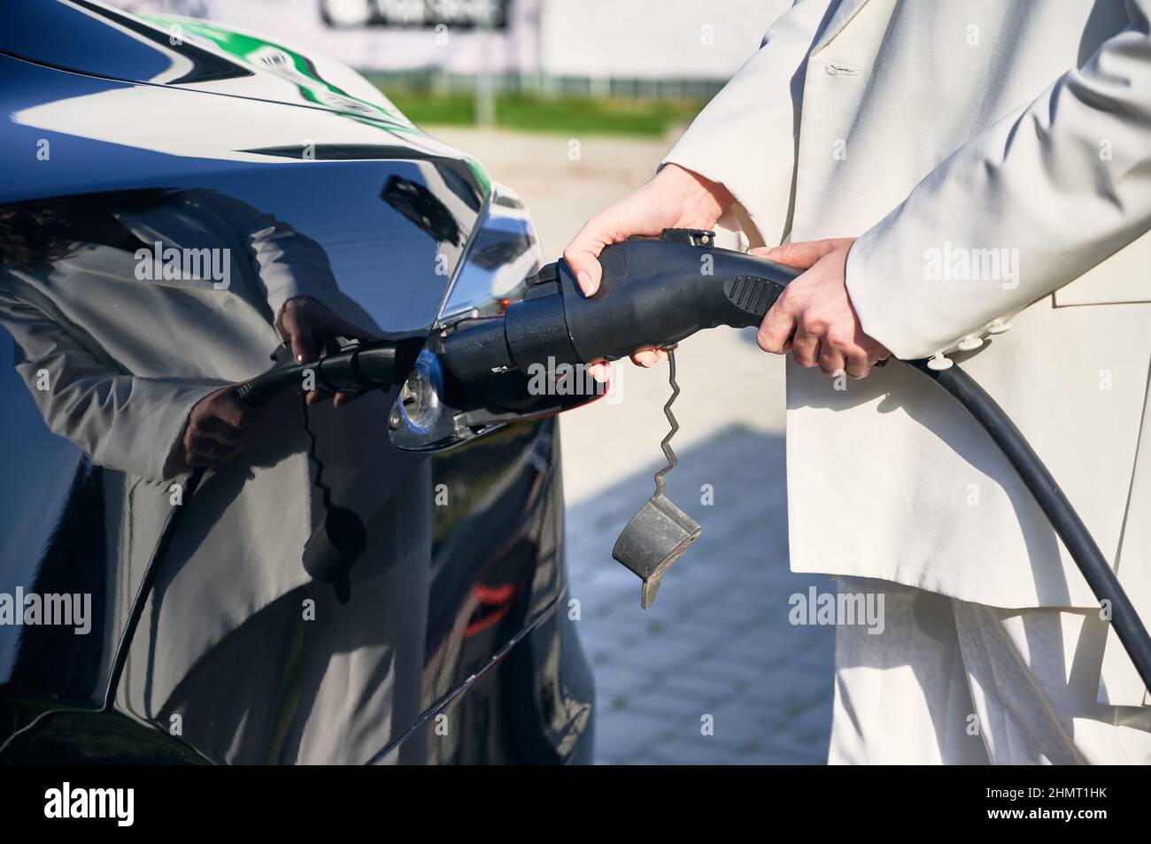 Vista ravvicinata delle mani della donna che collegano l'alimentatore all'auto elettrica. Carica di processo dei moderni veicoli elettrici ecologici. Energia alternativa per alimentare il trasporto. Foto Stock