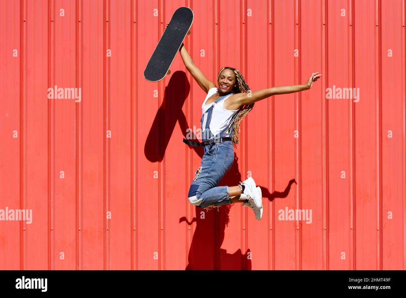 Donna nera spensierata con skateboard che salta in città Foto Stock