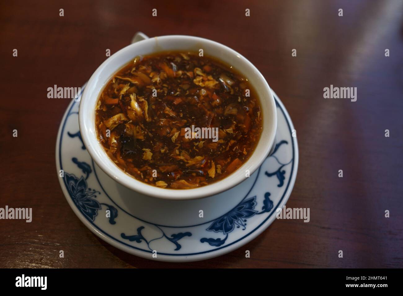 Zuppa cinese speziata e acida in una ciotola di porcellana bianca con motivo asiatico su un tavolo marrone scuro, spazio copia, fuoco selezionato, profondità di campo stretta Foto Stock