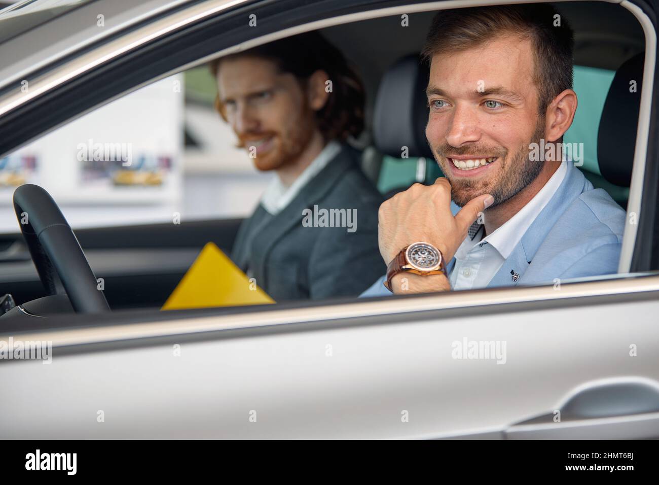 Un cliente è seduto in auto al negozio in un'atmosfera piacevole con un venditore e prova un veicolo che vuole comprare. Auto, negozio, acquisto Foto Stock