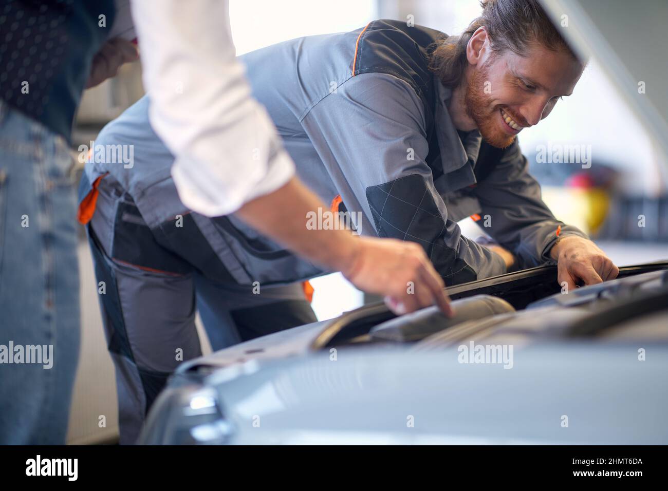 Un giovane meccanico in un'atmosfera di lavoro in officina sta controllando il motore dell'auto. Auto, meccanico, officina Foto Stock