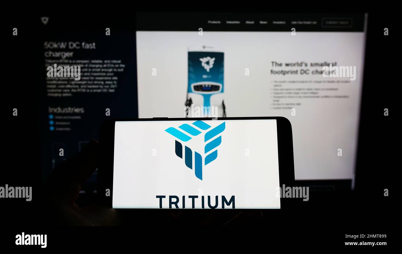 Persona che tiene uno smartphone con il logo della società di ricarica EV Trivium Holdings Pty Ltd sullo schermo di fronte al sito Web. Mettere a fuoco sul display del telefono. Foto Stock