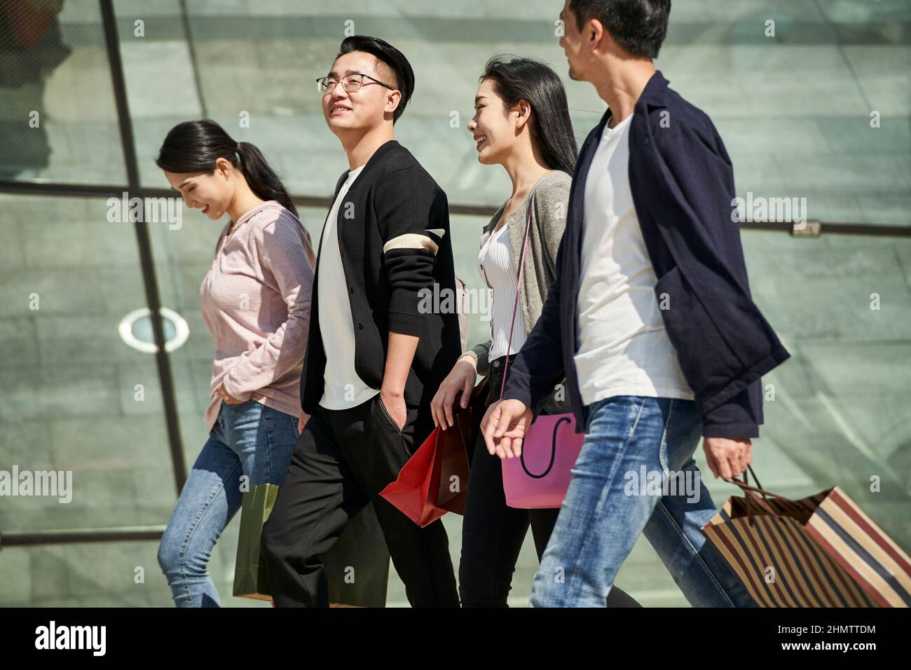 vista ad alto angolo di un gruppo di quattro giovani asiatici che chiacchierano parlando mentre si cammina per strada con borse shopping in mano Foto Stock