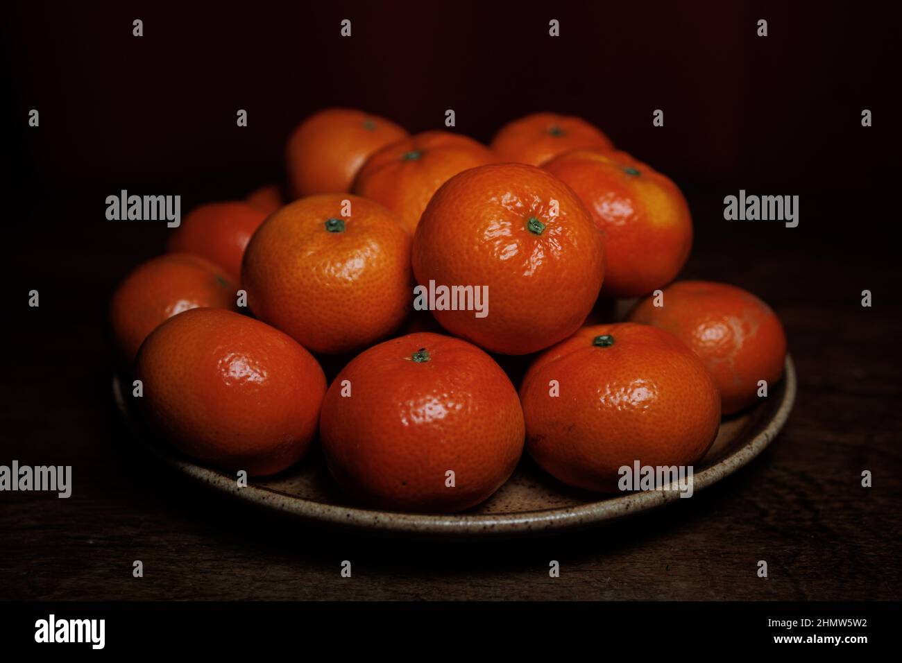 Molte arance mandarini su piatto e tavola di legno Foto Stock