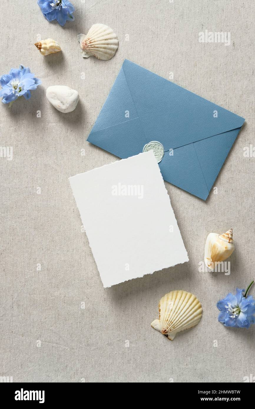 Biglietto d'invito per matrimoni nautici e busta con conchiglie e fiori blu su tavolo beige. Set di cancelleria per matrimoni. Mare, mare, stile acqua. Piatto l Foto Stock
