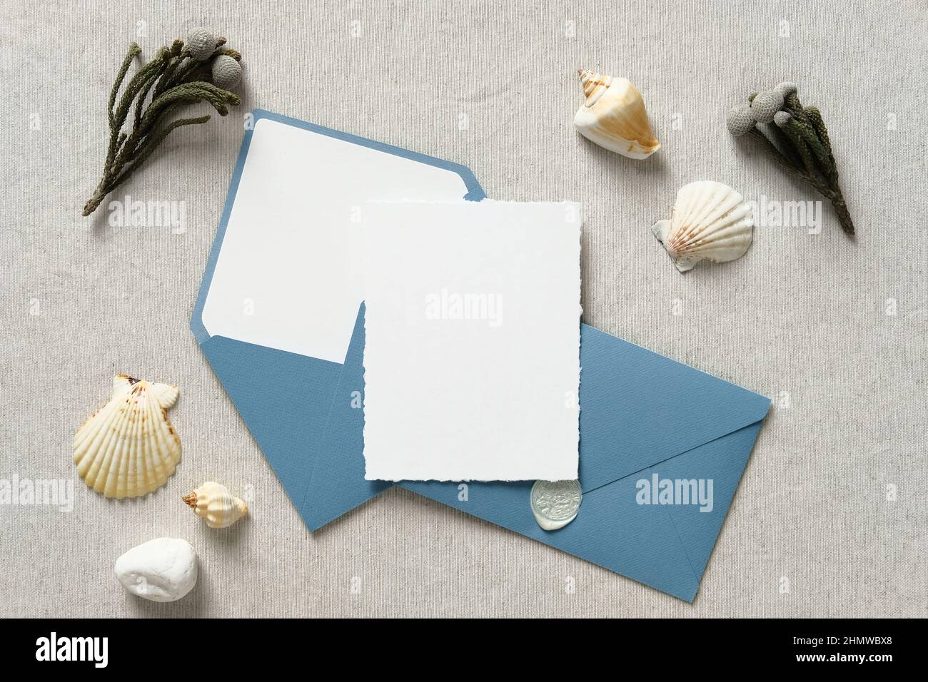 Mockup carta invito matrimonio nautico con buste blu, fiori, conchiglia su tavolo beige. Disposizione piatta, vista dall'alto, spazio di copia. Foto Stock