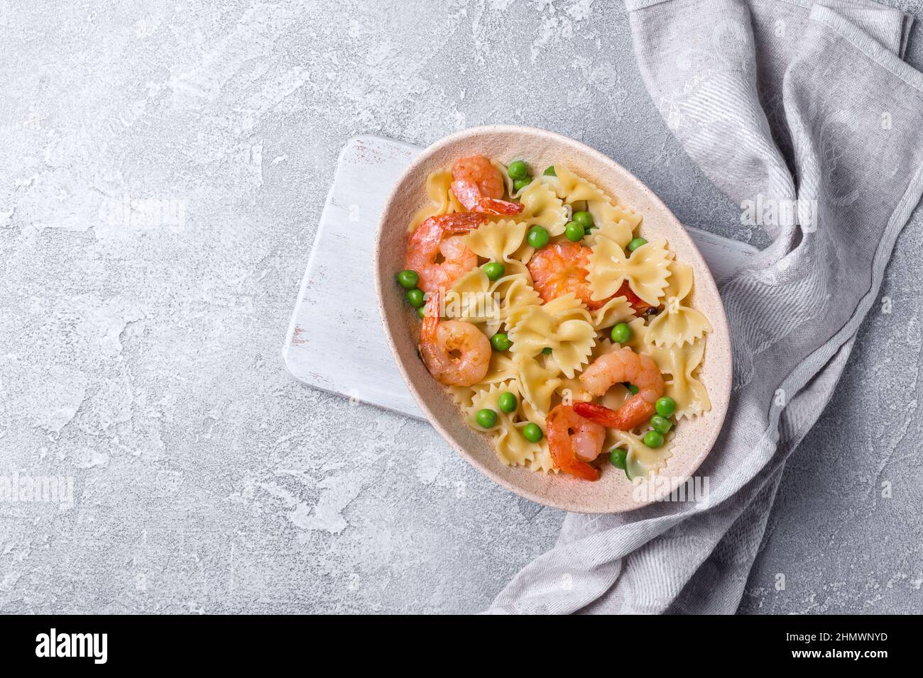 Vista dall'alto della gustosa pasta di farfalle italiana con gamberi o gamberi e piselli verdi su sfondo grigio di cemento Foto Stock