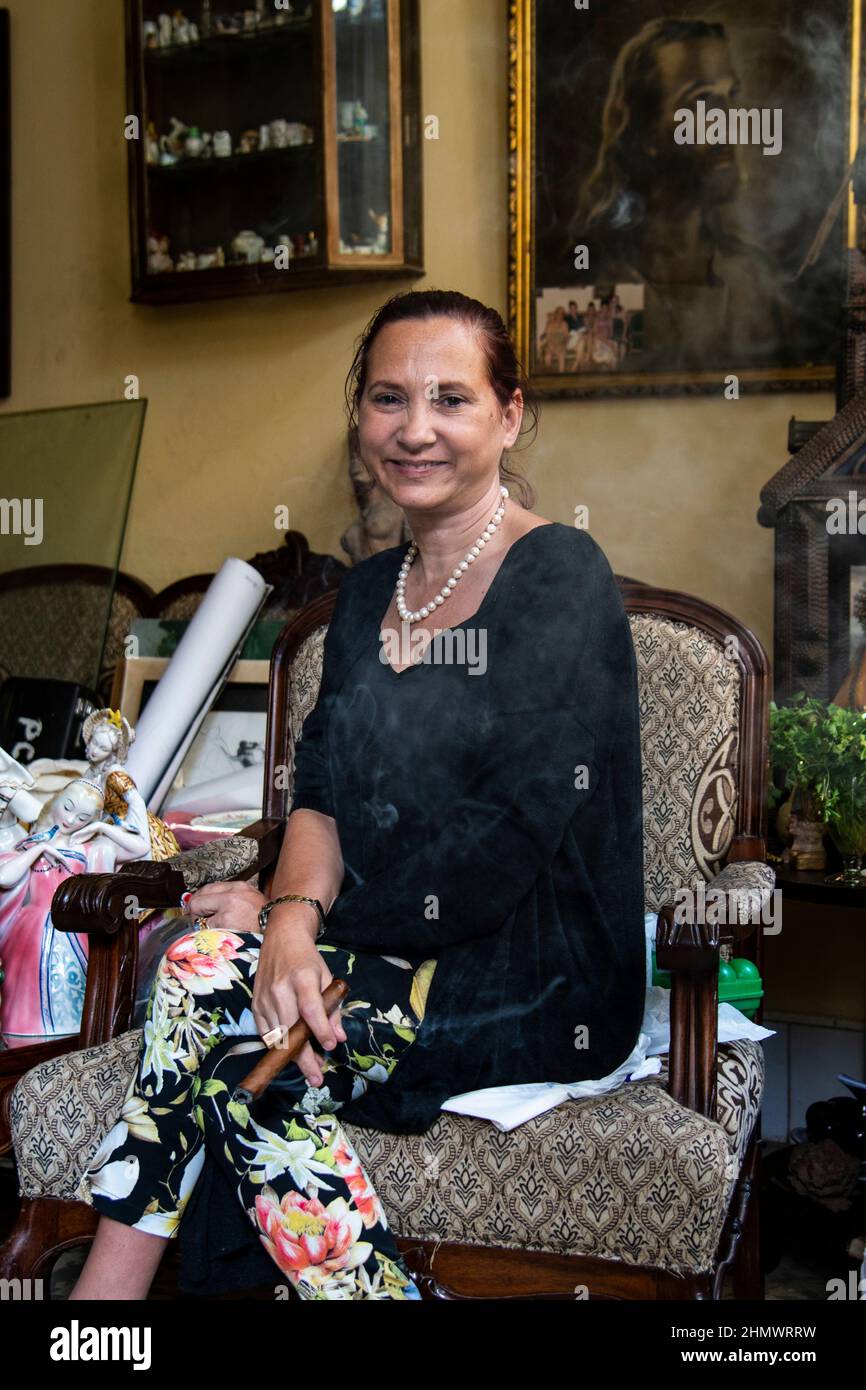 Una donna sorridente tiene in mano il sigaro cubano al suo negozio di antiquariato e d'epoca a l'Avana, Cuba. Foto Stock