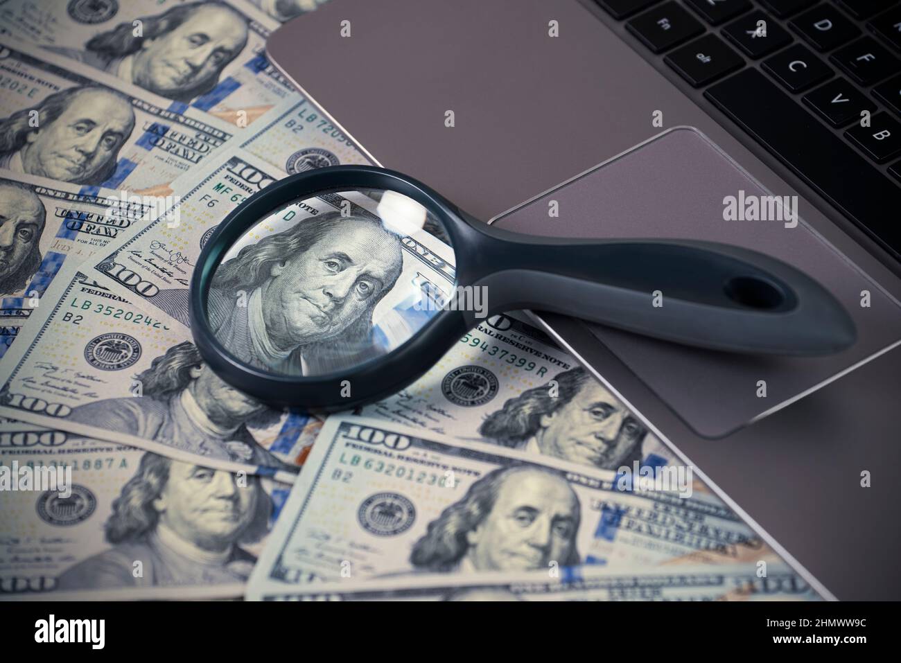 Laptop e lente d'ingrandimento su di noi bollette dollaro, primo piano Benjamin Franklin ritratto, fare soldi online concetto Foto Stock