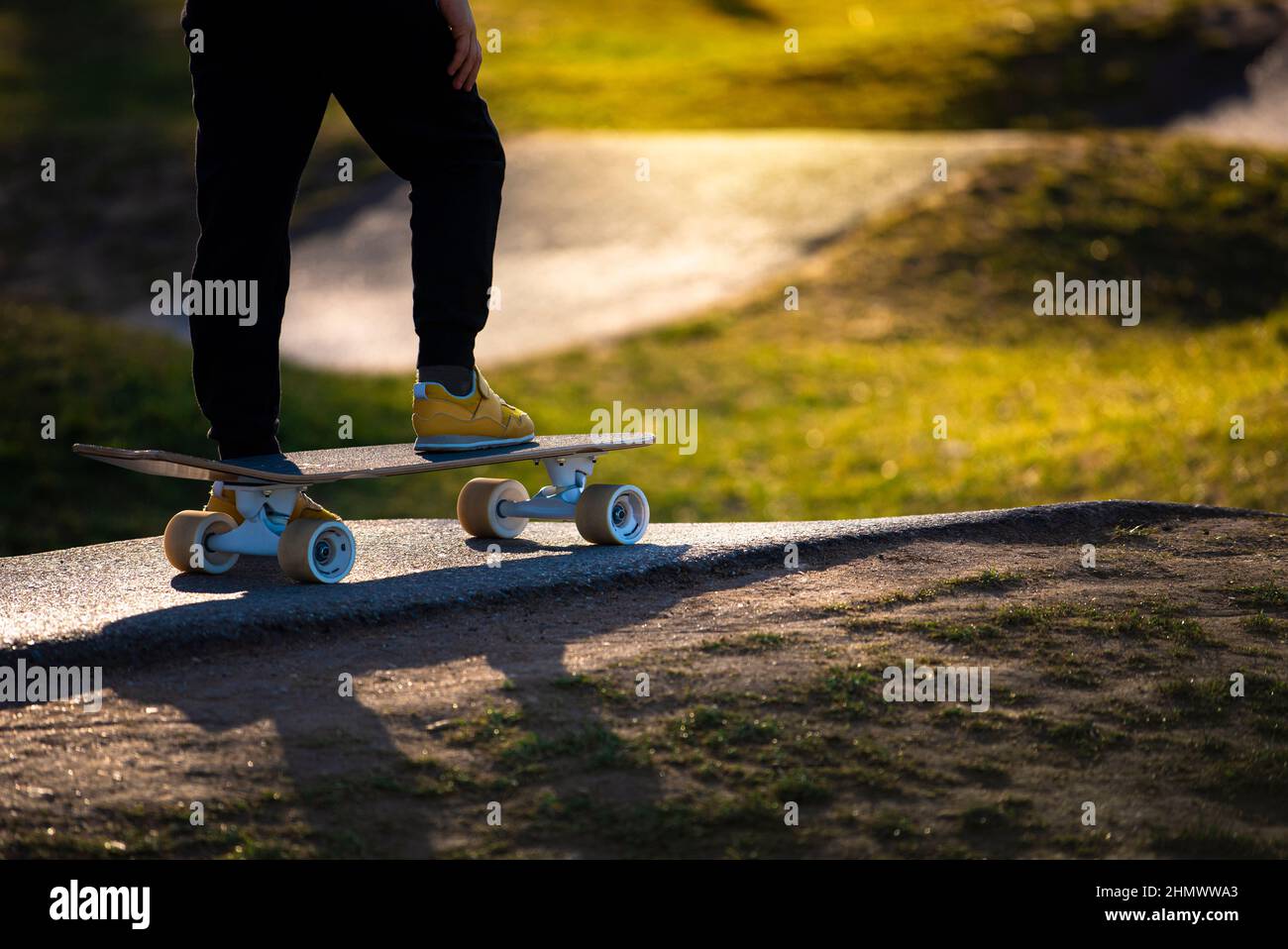 Gambe in sneakers gialle su uno skateboard presso lo skatepark in serata a raggi di sole Foto Stock