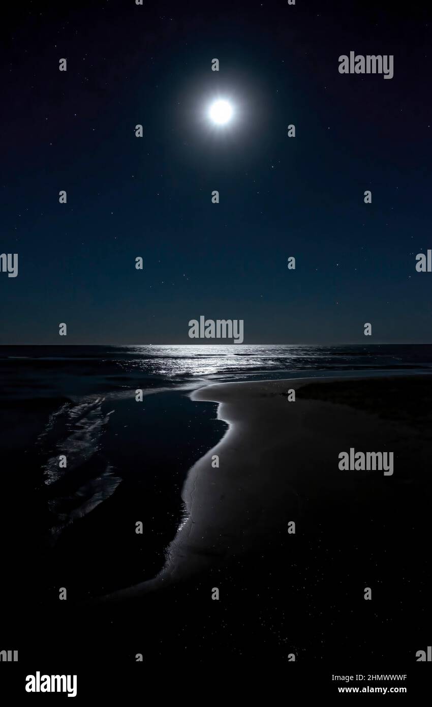 Immagine notturna di una spiaggia con la luna nel cielo stellato che riflette sull'acqua del litorale, dipingendo una grotta di luce, Isla Canela, Huelva Spagna, v Foto Stock