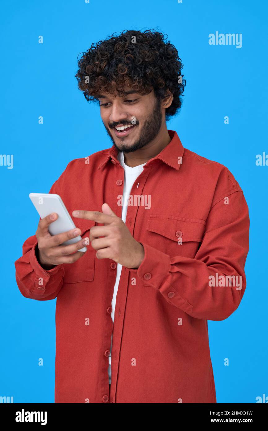 Felice uomo indiano giovane utilizzando cellulare isolato su sfondo blu. Foto Stock