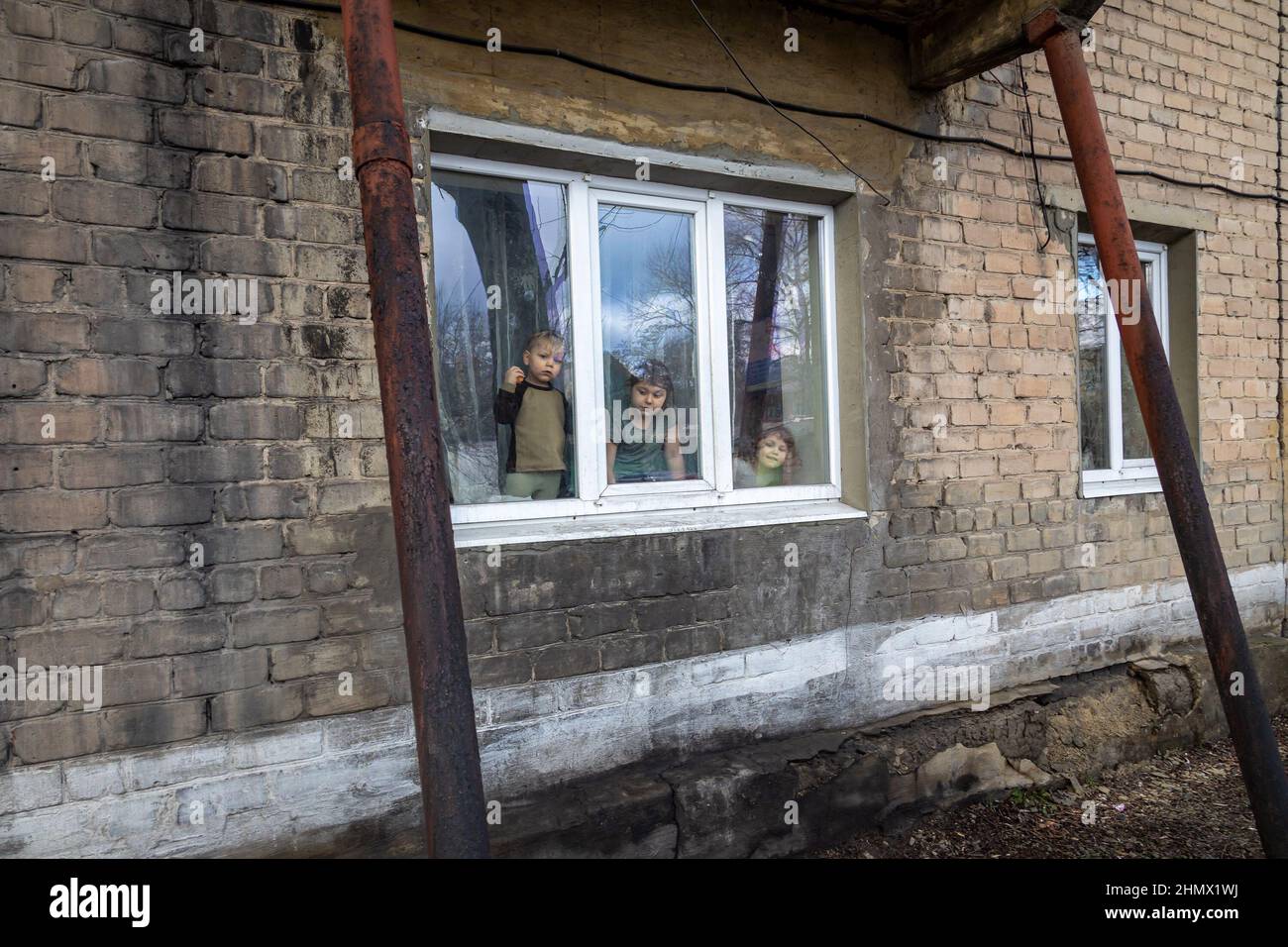 Gornyak, Ucraina. 9th Feb 2022. Tre dei bambini Mazur guardano fuori la finestra del loro appartamento il 9 febbraio 2022.9 febbraio 2022. Igor ed Eugenia Mazur, genitori di 5 bambini di età inferiore ai 8 anni, vivono a circa 10 miglia dalle linee di Donetsk a Gornyak, Ucraina. La famiglia lotta per trovare abbastanza lavoro per cibo e bollette e rimane preoccupata quando le forze militari russe si mobilitano sul confine ucraino. (Credit Image: © Michaal Nigro/Pacific Press via ZUMA Press Wire) Foto Stock