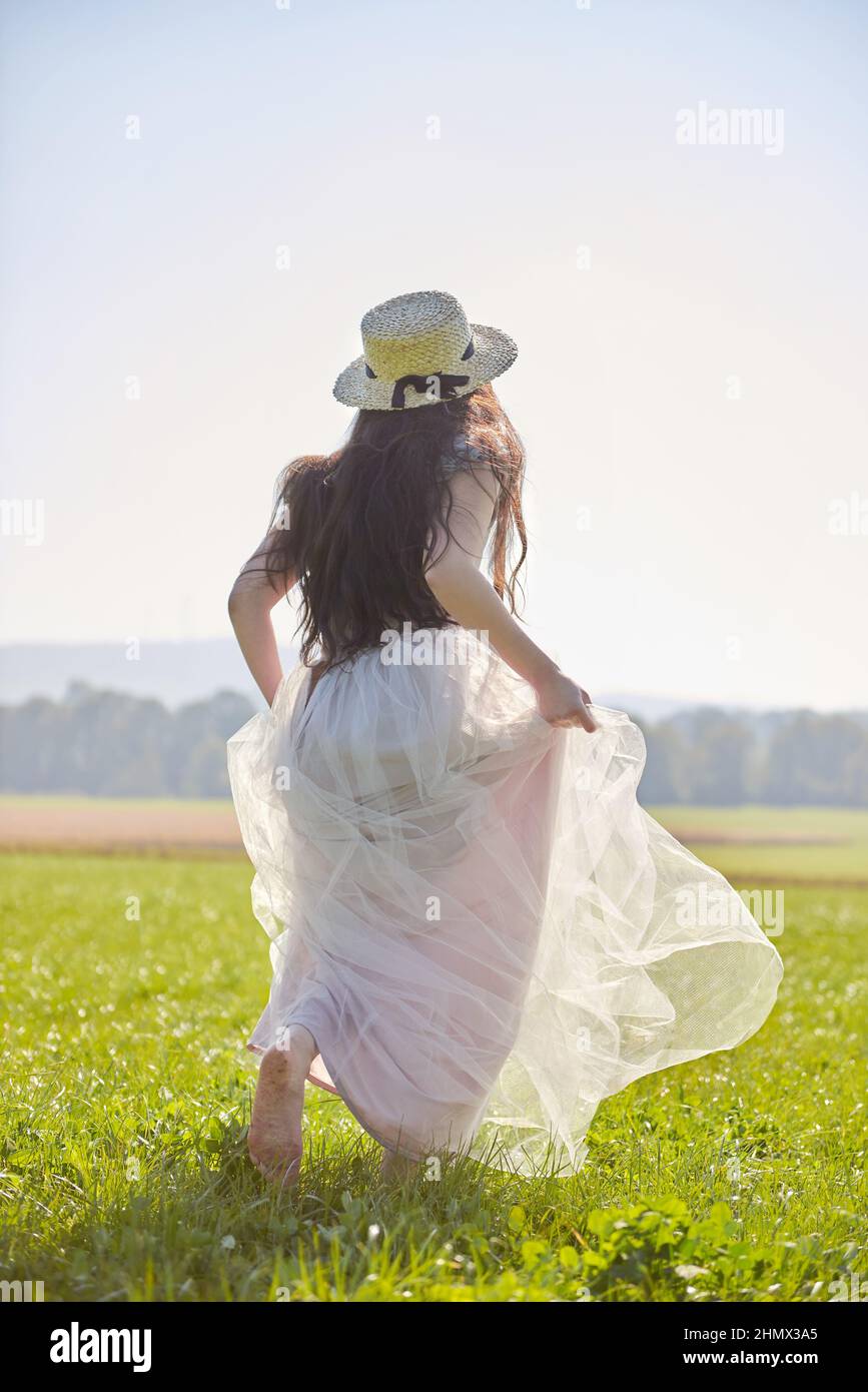 Giovane bella lunga capelli neri asiatica donna che indossa un abito romantico lilla in piedi in un campo d'erba retroilluminato Foto Stock