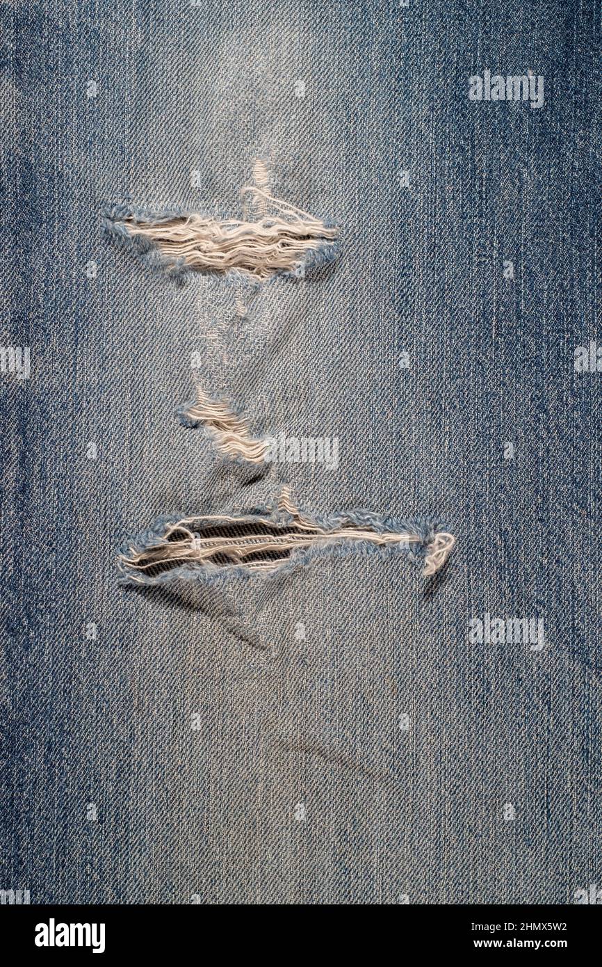 Particolare di tela di jeans blu strappata, con fori, stressata, sbiadita e danneggiata per backgraund Foto Stock