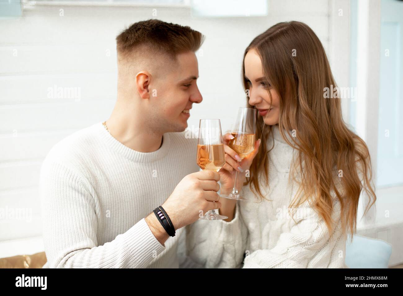 Giovane bella coppia a casa celebra la data di conoscenza, beve vino da bicchieri di vetro. Relazioni romantiche. Amore e tenerezza. Bellezza Foto Stock